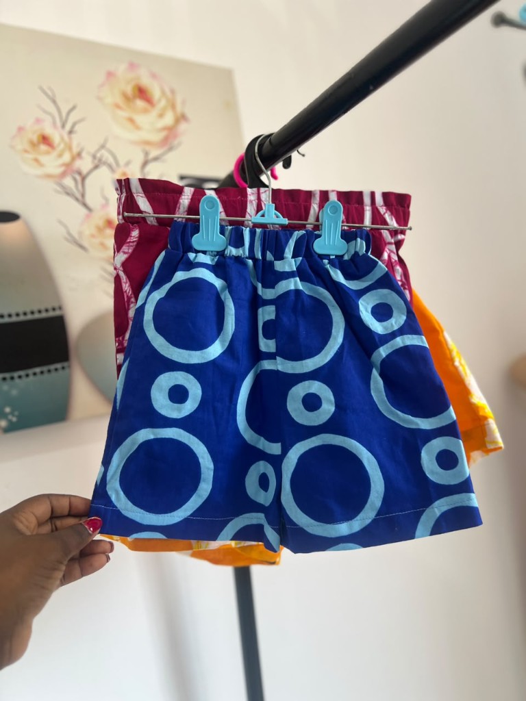 Children's indigo shorts in a pale circle print, held on a rail in the Accra atelier.
