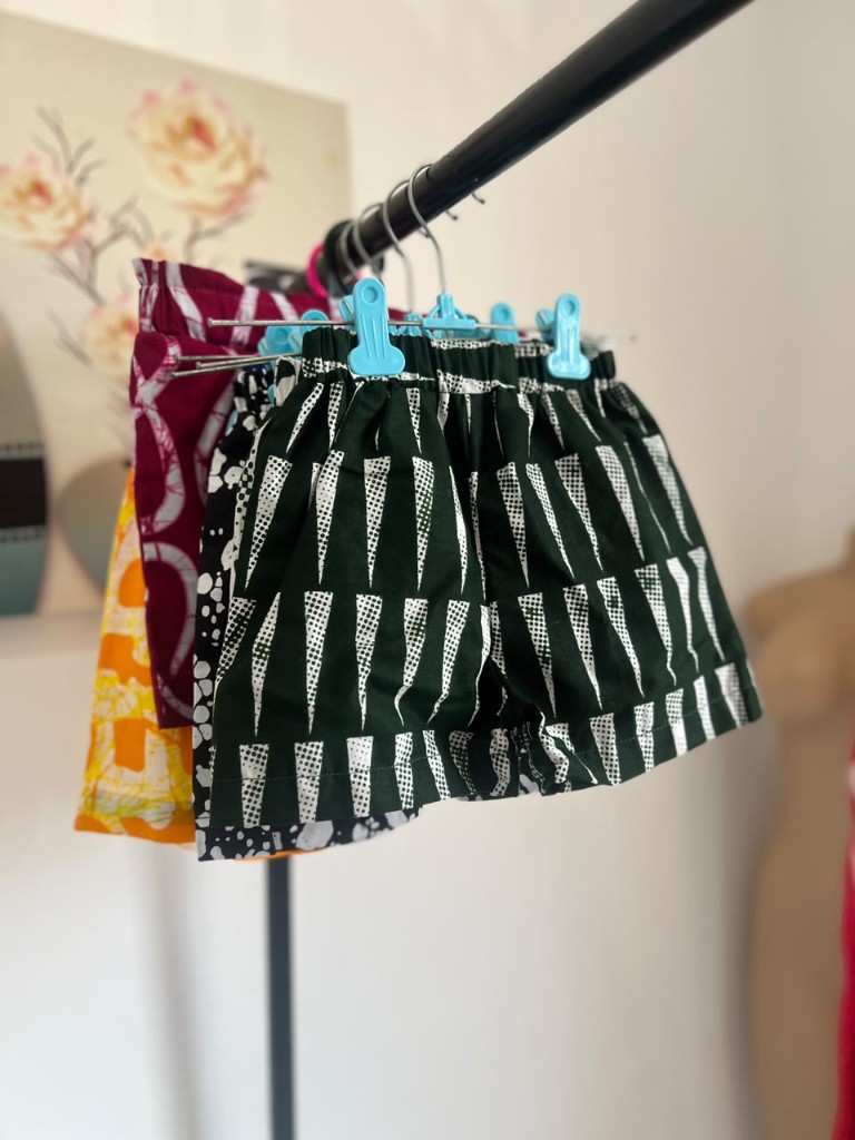 Children's forest-green shorts in a white triangle print, clipped on a rail.