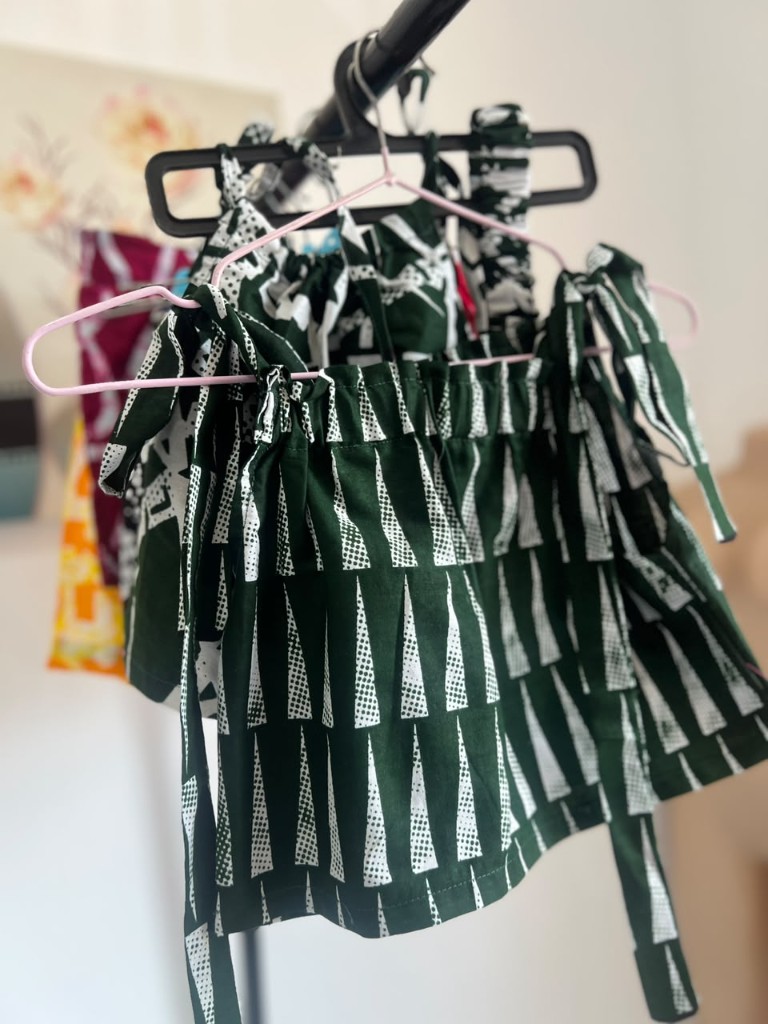 A child's forest-green tie-shoulder top in a white triangle print.